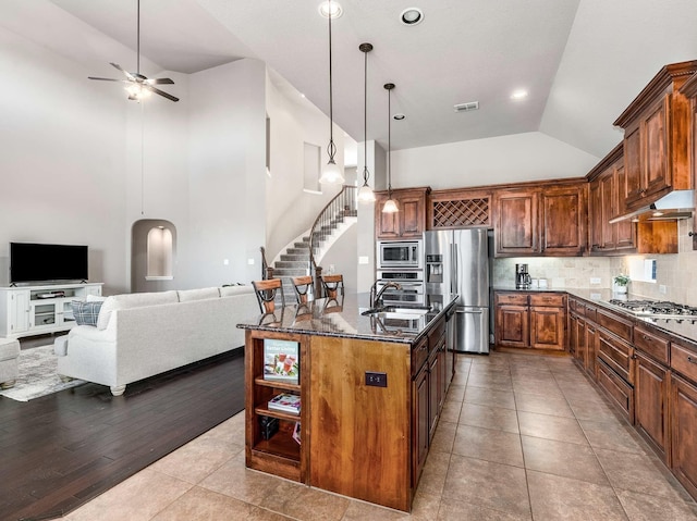 kitchen featuring visible vents, dark stone countertops, under cabinet range hood, open floor plan, and stainless steel appliances