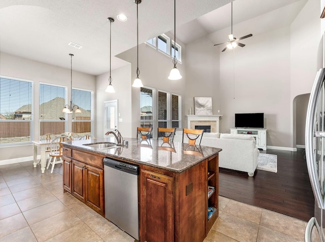 kitchen featuring a fireplace, a kitchen island with sink, a sink, appliances with stainless steel finishes, and ceiling fan with notable chandelier