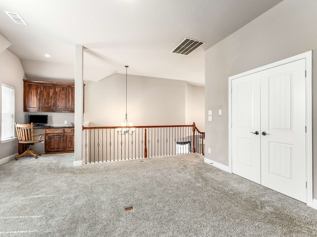 interior space with visible vents, baseboards, lofted ceiling, carpet floors, and built in desk