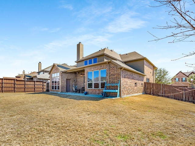 back of house featuring a lawn, brick siding, a fenced backyard, and a chimney