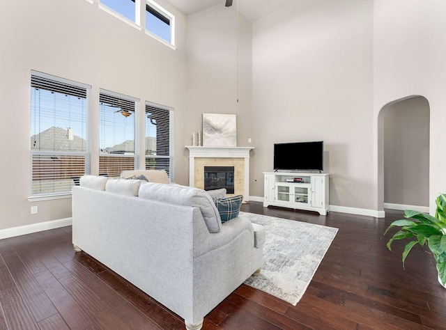 living area featuring dark wood finished floors, a glass covered fireplace, baseboards, and arched walkways