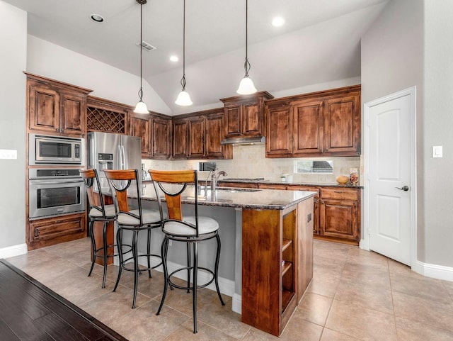 kitchen with under cabinet range hood, a sink, stainless steel appliances, decorative backsplash, and vaulted ceiling