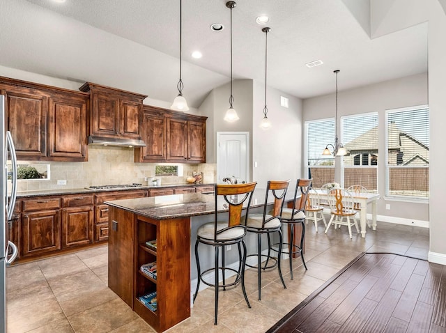 kitchen with a kitchen bar, visible vents, dark stone countertops, tasteful backsplash, and a center island