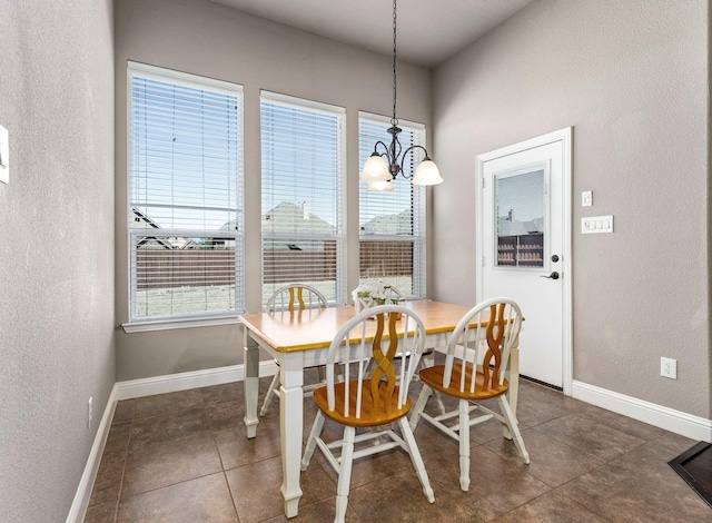 dining space featuring an inviting chandelier, dark tile patterned flooring, baseboards, and a textured wall