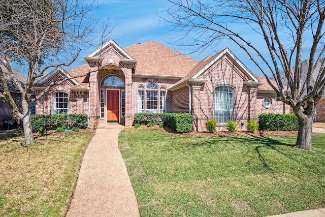 view of front of house with brick siding, a front yard, and roof with shingles