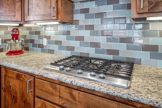 kitchen featuring stainless steel gas cooktop, tasteful backsplash, brown cabinetry, and light stone counters