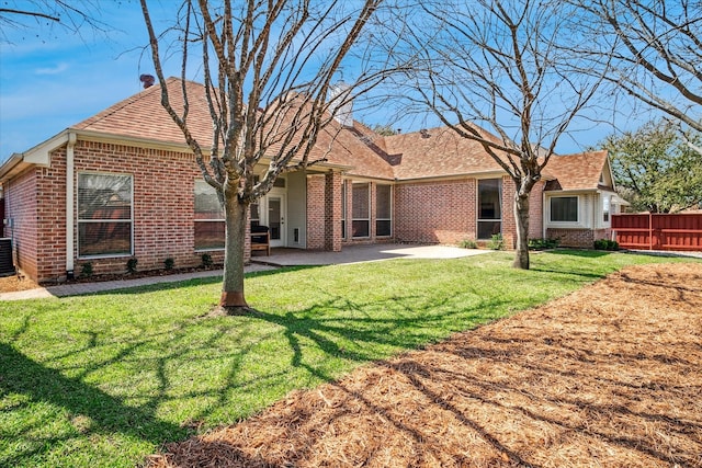 rear view of house featuring brick siding, fence, a lawn, cooling unit, and a patio