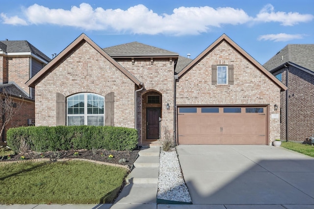 french country style house with brick siding, driveway, a garage, and roof with shingles