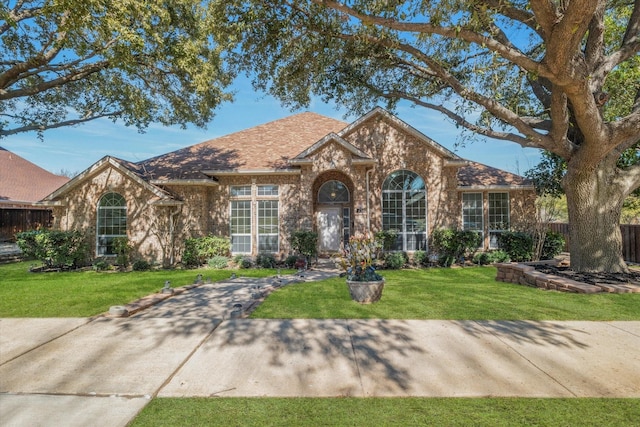 ranch-style home with brick siding, a shingled roof, a front lawn, and fence