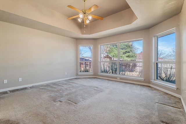 carpeted spare room with a tray ceiling, a ceiling fan, and baseboards