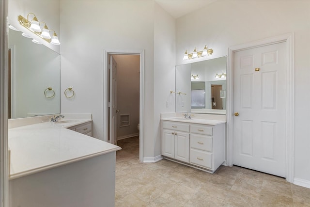 bathroom with toilet, two vanities, baseboards, and a sink