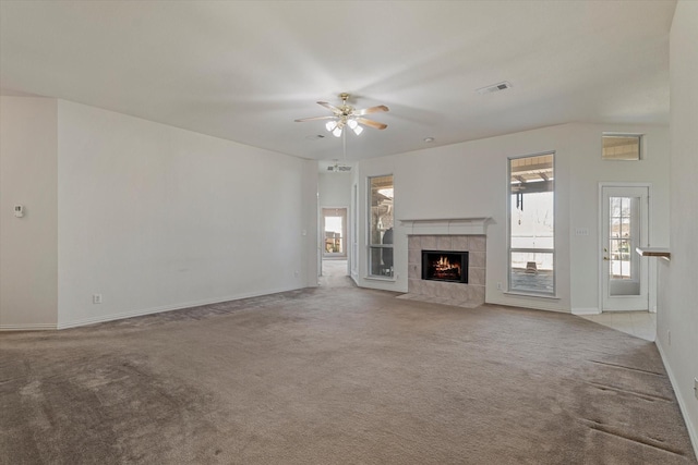 unfurnished living room with visible vents, a ceiling fan, a tiled fireplace, carpet flooring, and baseboards