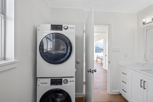 laundry room with laundry area, ornamental molding, stacked washer / drying machine, and wood finished floors