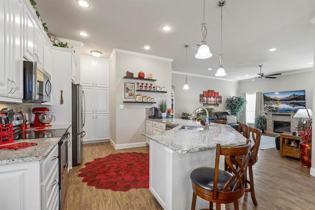 kitchen with a sink, stainless steel appliances, white cabinets, open floor plan, and light wood-type flooring