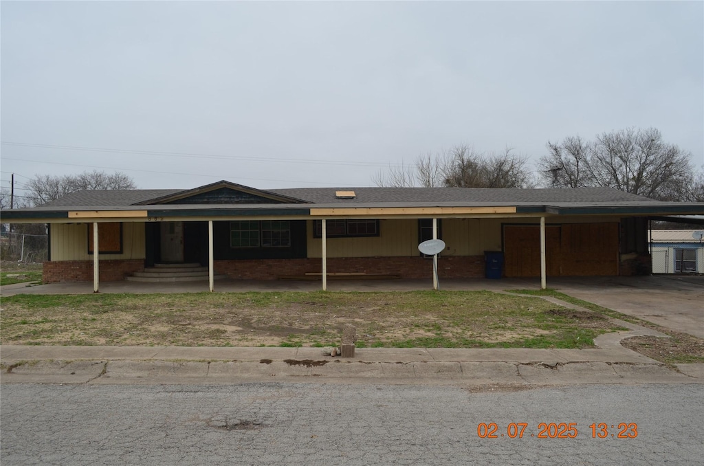 ranch-style house featuring brick siding, an attached carport, driveway, and a shingled roof