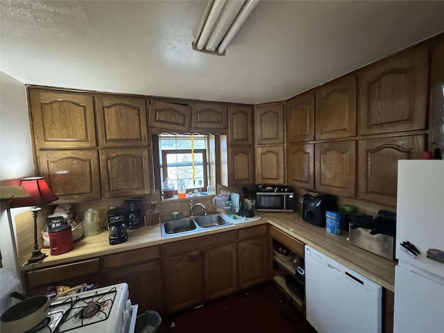 kitchen with brown cabinetry, white appliances, light countertops, and a sink