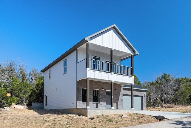 view of front of house featuring a balcony, brick siding, concrete driveway, a garage, and board and batten siding