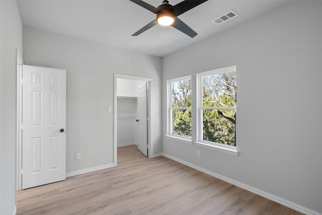 unfurnished bedroom with baseboards, visible vents, light wood finished floors, ceiling fan, and a walk in closet