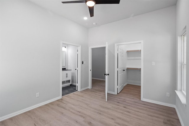 unfurnished bedroom with light wood-style flooring, ensuite bath, a walk in closet, and baseboards