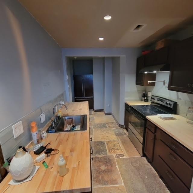 kitchen featuring stone tile floors, stainless steel electric range, a sink, black refrigerator, and wall chimney exhaust hood