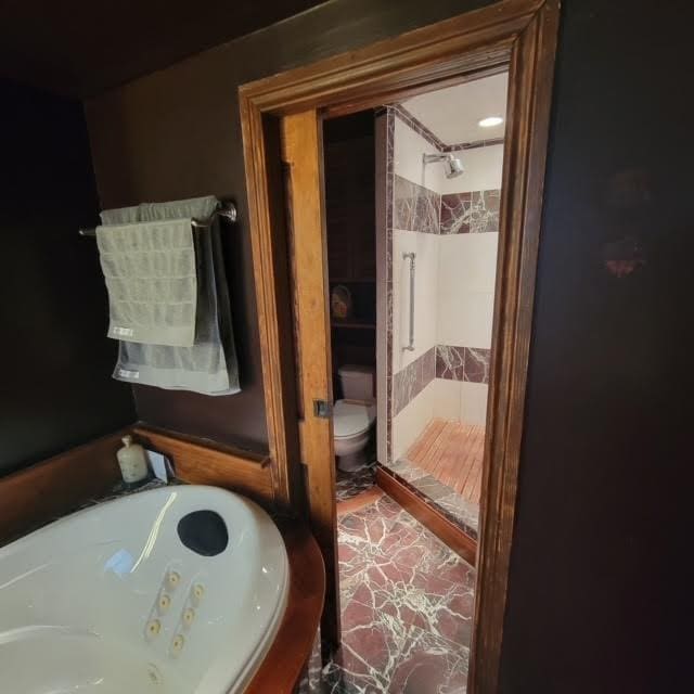 bathroom featuring toilet, a tub with jets, and a shower stall