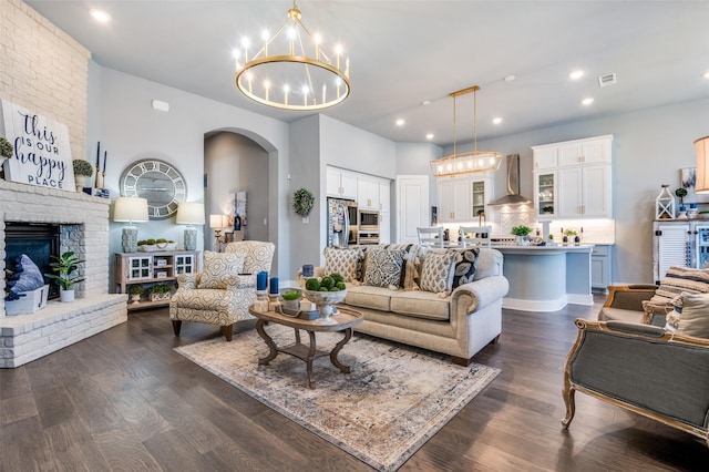 living room with a chandelier, visible vents, arched walkways, dark wood finished floors, and a brick fireplace