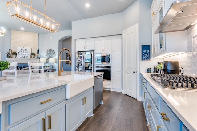 kitchen with decorative backsplash, appliances with stainless steel finishes, exhaust hood, arched walkways, and a sink