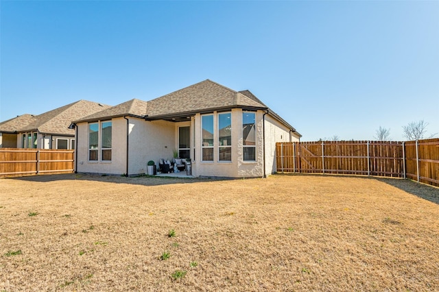 back of house featuring brick siding, a fenced backyard, a shingled roof, and a yard