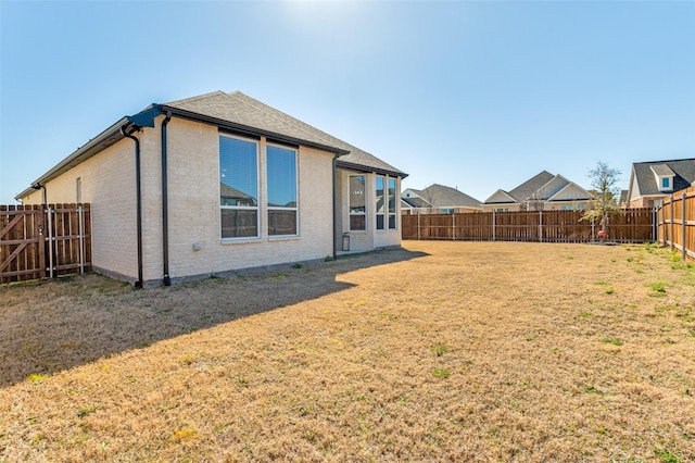 exterior space with roof with shingles, a yard, brick siding, and a fenced backyard