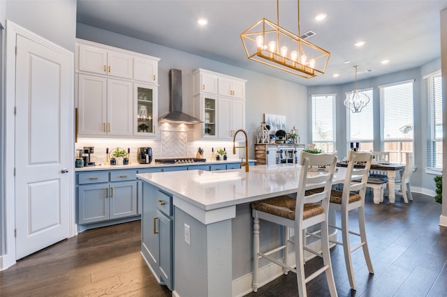 kitchen with wall chimney range hood, stainless steel gas stovetop, light countertops, dark wood-style flooring, and a notable chandelier