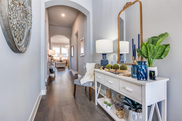hallway featuring dark wood-style flooring, baseboards, and arched walkways