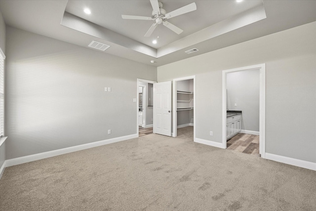 unfurnished bedroom with a tray ceiling, visible vents, baseboards, and light carpet