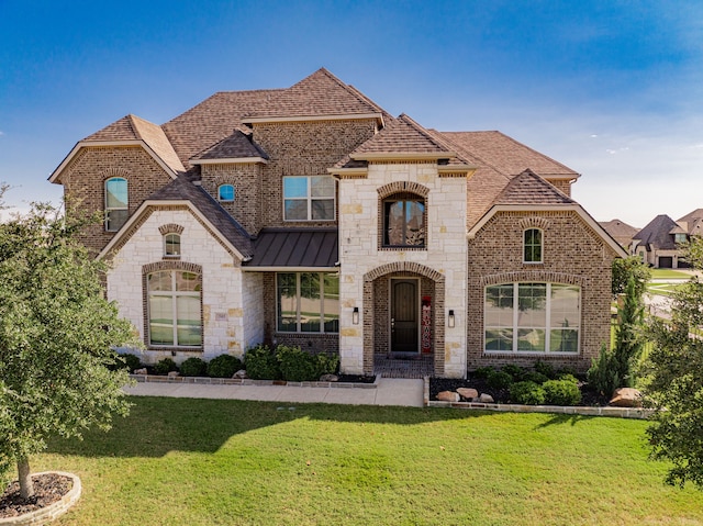 french country style house with brick siding, a standing seam roof, a front lawn, and roof with shingles