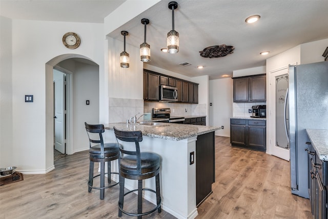 kitchen featuring a sink, arched walkways, appliances with stainless steel finishes, a peninsula, and dark brown cabinets