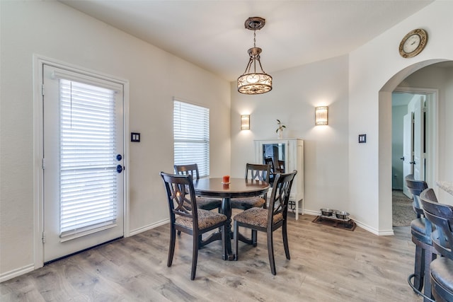 dining room with arched walkways, light wood-type flooring, and baseboards