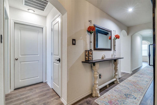 corridor featuring wood finished floors, arched walkways, visible vents, and baseboards