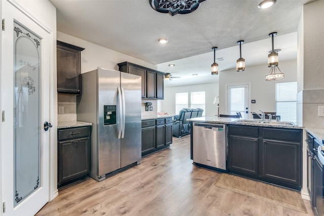 kitchen featuring light stone countertops, a peninsula, a sink, appliances with stainless steel finishes, and light wood-type flooring