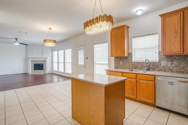 kitchen with a sink, stainless steel dishwasher, a center island, a fireplace, and light tile patterned floors