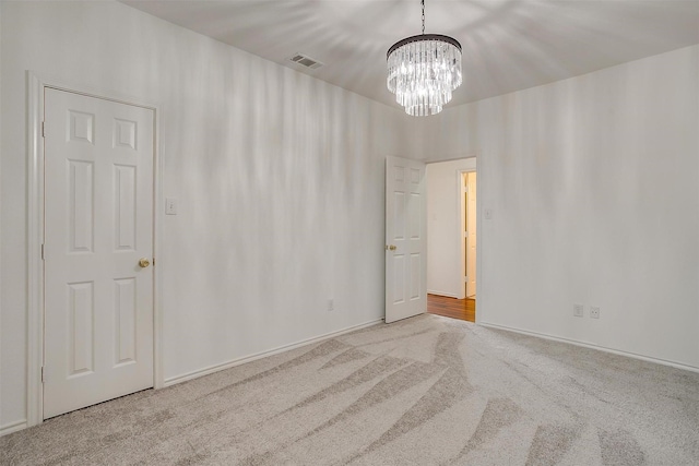 carpeted spare room with visible vents and a chandelier