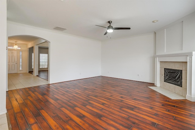 unfurnished living room featuring visible vents, ornamental molding, a tiled fireplace, wood finished floors, and arched walkways