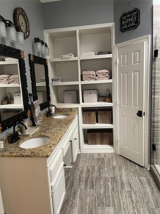 bathroom with a sink, double vanity, wood finished floors, and a shower stall