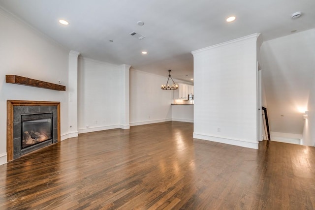 unfurnished living room with dark wood-style floors, visible vents, ornamental molding, a glass covered fireplace, and a notable chandelier