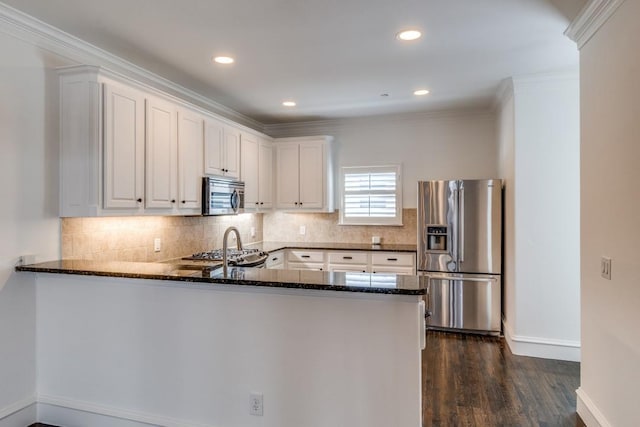 kitchen with dark stone countertops, a peninsula, appliances with stainless steel finishes, white cabinets, and decorative backsplash