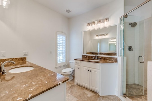 full bath featuring toilet, a shower stall, two vanities, and a sink