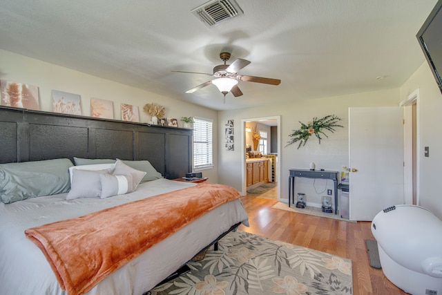 bedroom with visible vents, ensuite bath, light wood-type flooring, and a ceiling fan