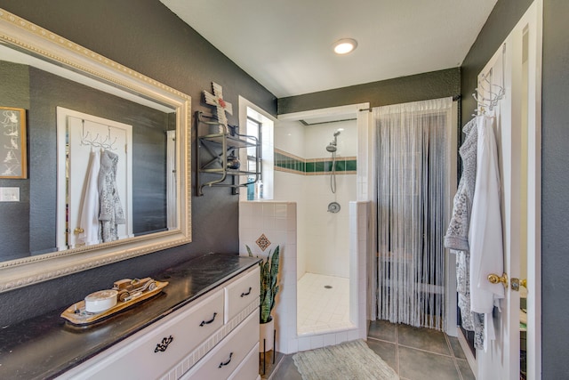 bathroom featuring vanity, a textured wall, tile patterned flooring, and a tile shower