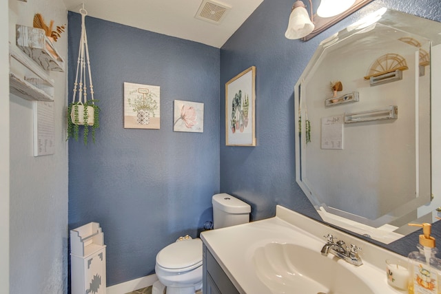 half bath featuring visible vents, toilet, vanity, and a textured wall