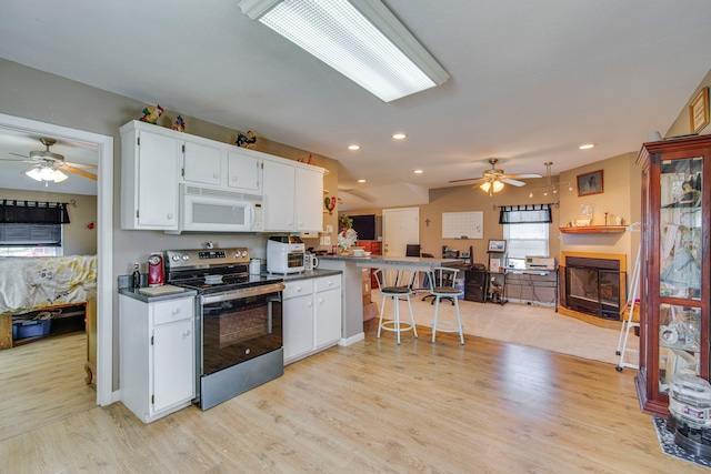 kitchen with white microwave, a breakfast bar area, stainless steel range with electric cooktop, light wood-style floors, and white cabinetry