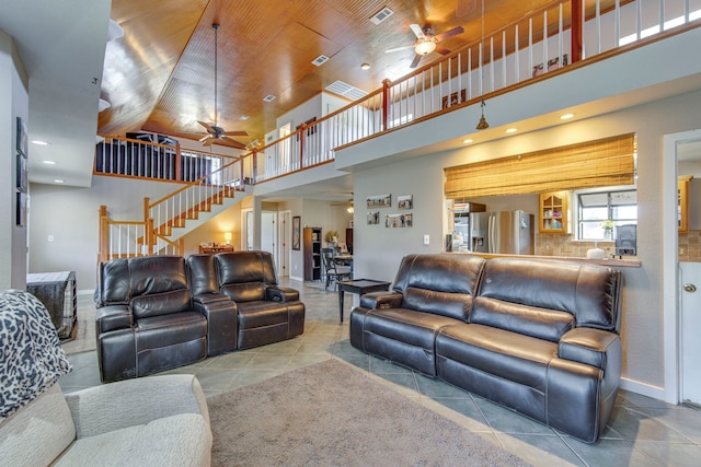 tiled living room featuring visible vents, a ceiling fan, stairway, baseboards, and a towering ceiling