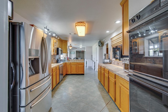 kitchen with stainless steel appliances, backsplash, a peninsula, and light tile patterned flooring